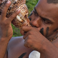 A Fijian man blows a conch shell to summon guests to a ceremony.